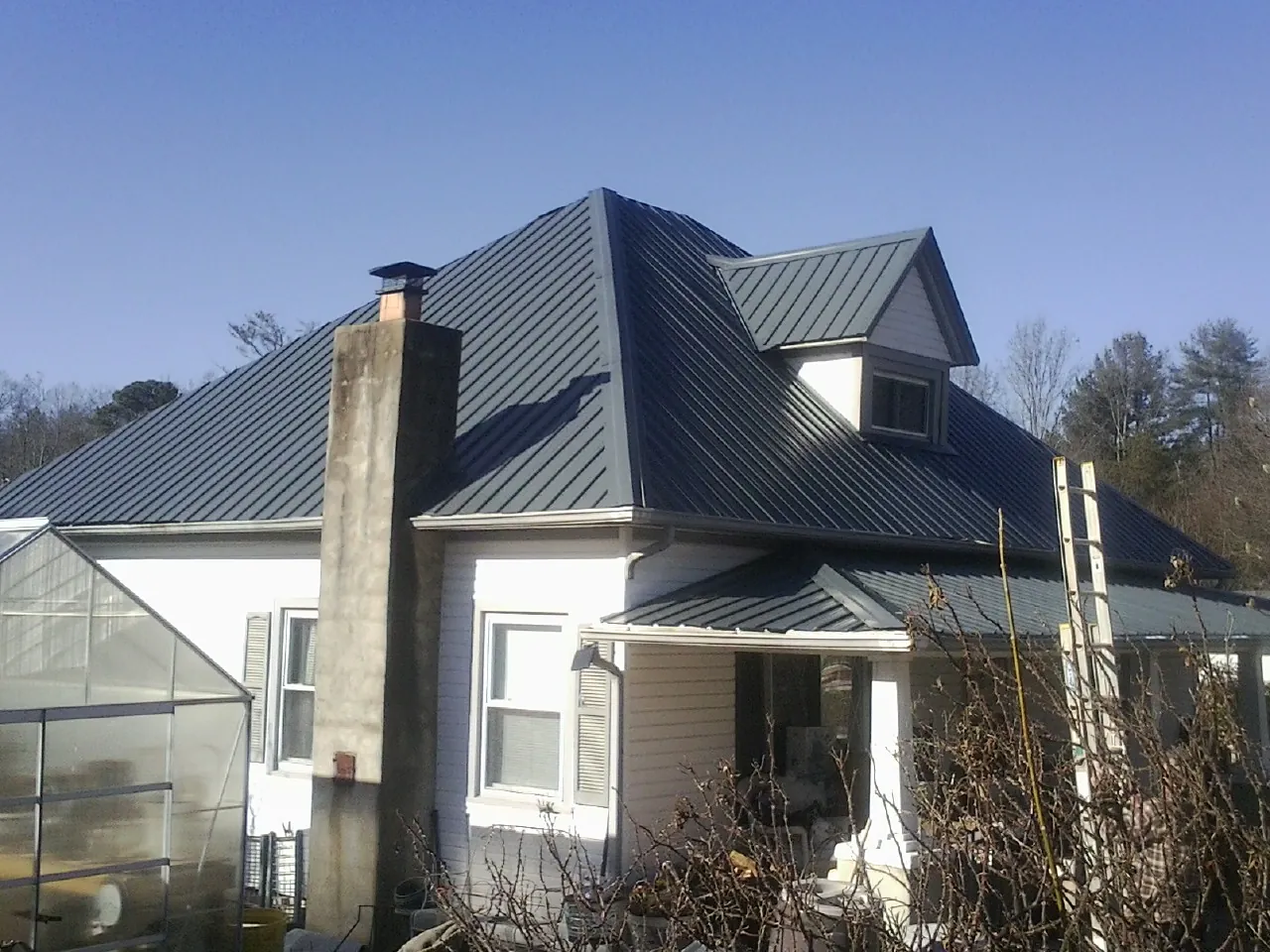 Dark blue standing seam metal roof on a white farmhouse with dormer — Slate & Tile Roof Repair by Roofing Brothers in Ossipee