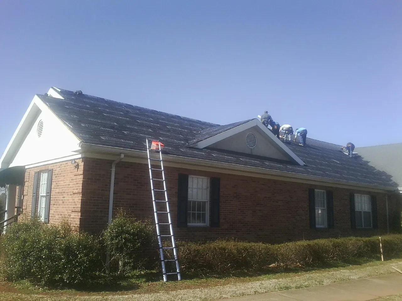Crew tearing shingles off a brick ranch roof with a ladder set — Metal Roof Repair work by our crew in Ossipee