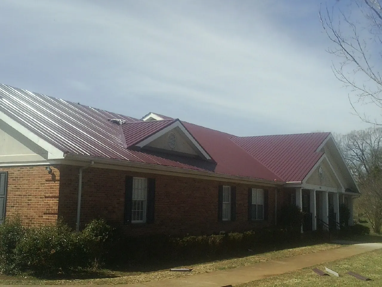 Red metal roof with gabled entries on a long brick building, from a Hail Damage Roof Repair job in Ossipee