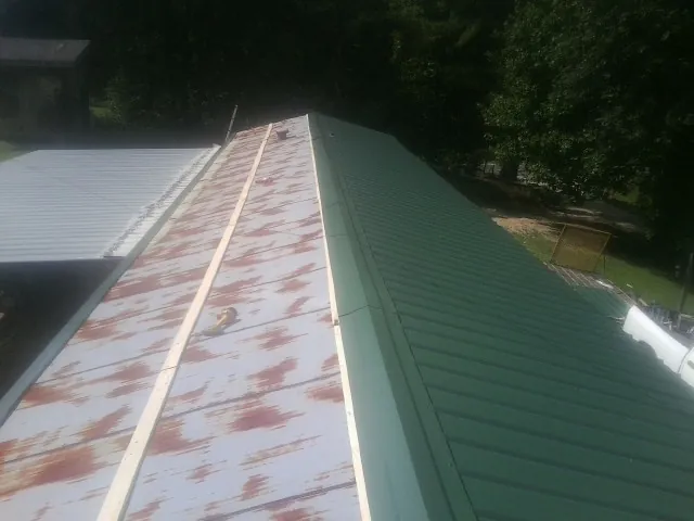 Old rusted panels beside newly installed green metal roofing — Wind Damage Roof Repair by Roofing Brothers in Ossipee