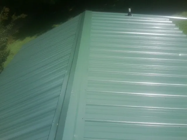 New green metal panels meeting at the ridge of a roof — Flat Roof Repair work by our crew in Ossipee