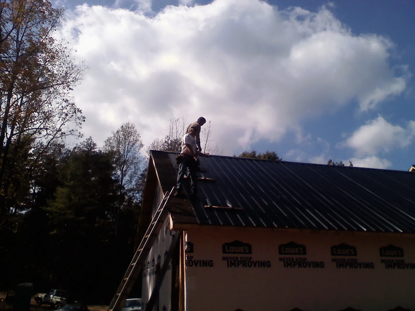 Roofer fastening dark metal panels high against a cloudy sky, from a Roof Inspection job in Ossipee