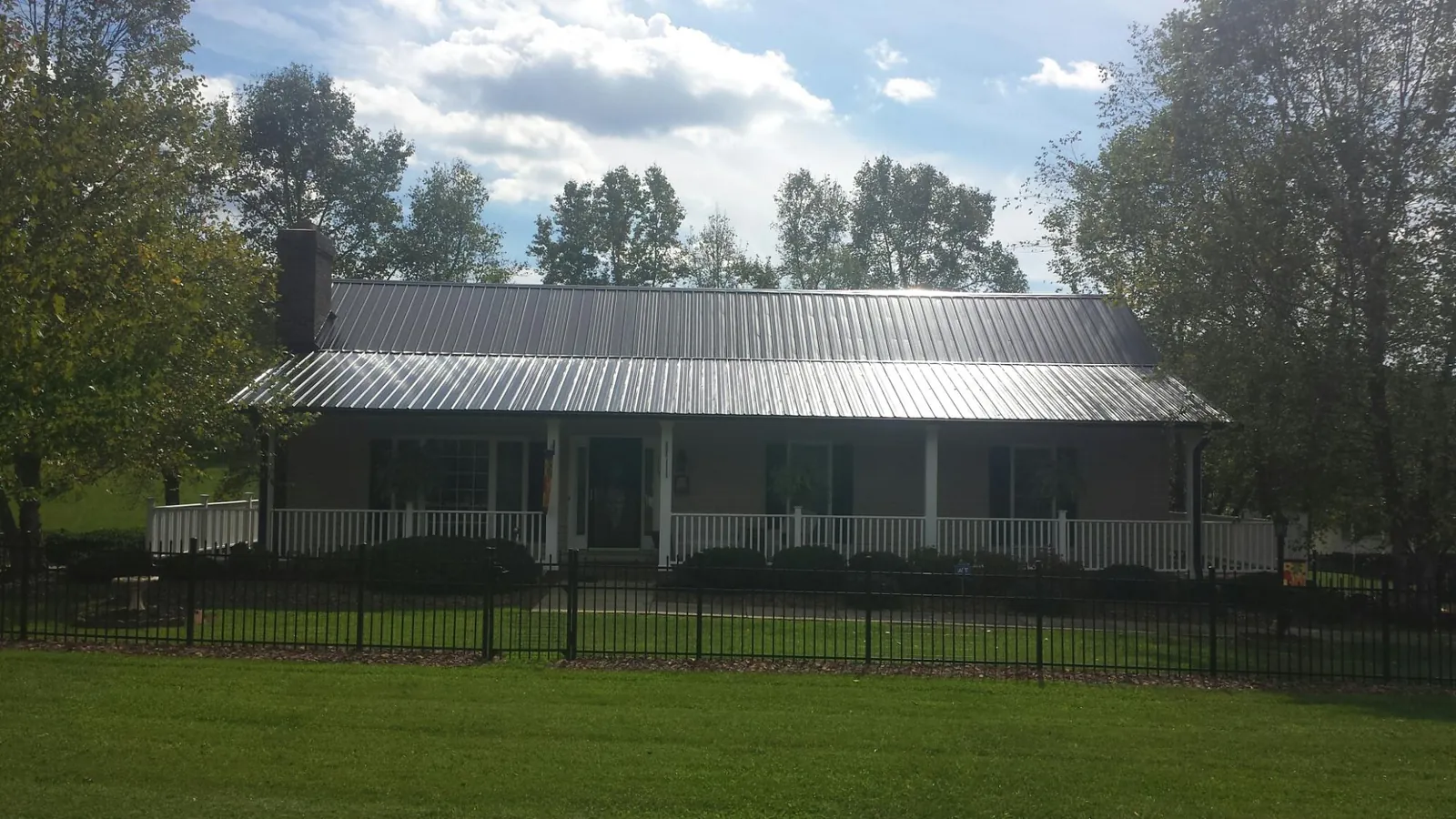 Gray metal roof on a brick ranch with a full width front porch — Gutter Guard Installation work by our crew in Ossipee