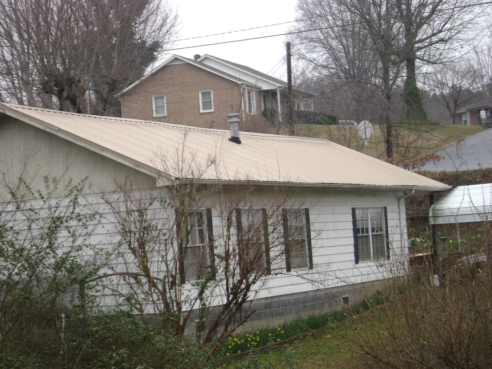 Tan metal roof on a white sided house set into a hillside — Commercial Roofing by Roofing Brothers in Ossipee
