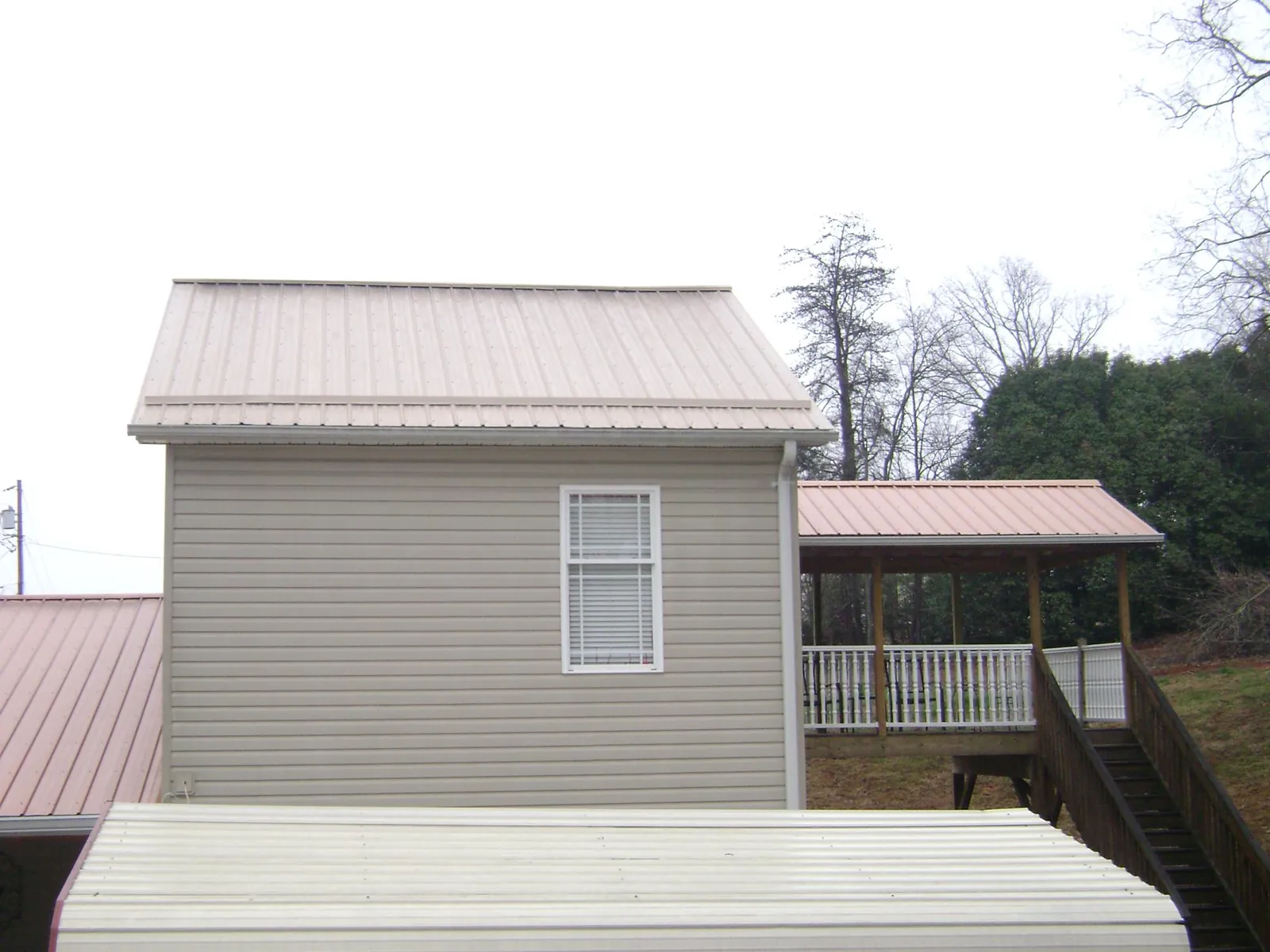 Tan metal roofs on a two story addition and attached porch, from a Roof Replacement job in Ossipee